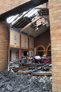 Overcast sunlight filters through the gaps of the burned roof onto the ashes and clutter of St. Monica Parish&rsquo;s narthex on Sept. 9. Fire destroyed the narthex of the northwest side Indianapolis church earlier that morning. (Photo by Natalie Hoefer)