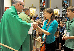 Msgr. William Stumpf, archdiocesan vicar general, gives Communion to Samantha McGuire, a member of St. Martin of Tours Parish in Martinsville, during a Sept. 25 Mass in the upper church of St. John the Evangelist Church in Philadelphia. Preparing to receive Communion next is McGuire&rsquo;s son, Joseph. They were among 46 Catholics from central and southern Indiana who participated in the World Meeting of Families in Philadelphia from Sept. 22-25. (Photo by Sean Gallagher)
