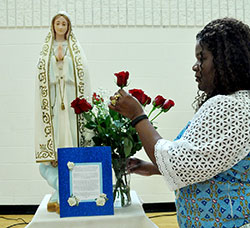 Dabrice Bartet, one of the coordinators of a 33 Days to Morning Glory Marian consecration group study at St. Monica Parish in Indianapolis, adjusts a bouquet of roses next to the statue of Mary used during the group&rsquo;s consecration service on Sept. 12 in the parish&rsquo;s gym. (Photos by Natalie Hoefer)