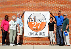 Volunteers for the Indianapolis council of the Society of St. Vincent de Paul stand with a &ldquo;Mission 27 Resale Coming Soon&rdquo; sign on July 11 outside of the thrift store&rsquo;s soon-to-be home at 1201 E. Maryland St. in Indianapolis. The volunteers are Changing Lives Forever director Domini Rouse, left, distribution intake manager Barbara Niezgodski, president John Ryan, linens and bedding coordinator Kathleen Williams, distribution center executive director Jeff Blackwell and south district council president Charlie Mazza. (Photo by Natalie Hoefer)