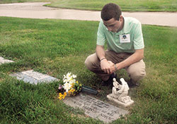 Seminarian Liam Hosty spends time on Aug. 10 before the grave of Father Joseph MacNally at Calvary Cemetery in Indianapolis. Hosty and other archdiocesan seminarians did various works of mercy, including praying for the dead, during their recent annual convocation. Father MacNally was Hosty&rsquo;s boyhood pastor at St. Barnabas Parish in Indianapolis. (Photo by Sean Gallagher)