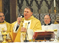 Cardinal Joseph W. Tobin elevates the Eucharist during a Nov. 20 liturgy in the Church of St.&nbsp;Alphonsus Liguori in Rome. Standing behind him is Loral Tansy, master of ceremonies. (Photo by John Shaughnessy) 