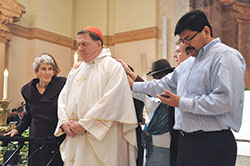 Deacon candidate Juan Carlos Ramirez, right, recites from a prayer card as he, Marie Tobin, left, Domini Rouse and Benedictine Sister Jennifer Mechtild Horner lay their hands upon and pray for Cardinal&nbsp;Joseph W. Tobin in front of the altar at SS. Peter and Paul Cathedral in Indianapolis as part of a prayer and blessing of him during the cardinal&rsquo;s farewell Mass on Dec. 3. (Photo by Natalie Hoefer)