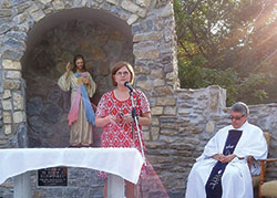 Mary Rose Carlow, a member of Prince of Peace Parish in Madison, speaks on Oct. 4 about the Divine Mercy image during a dedication ceremony for the parish&rsquo;s new grotto, an effort she envisioned, raised funds for and coordinated. Prince of Peace pastor Father Christopher Craig sits at right. (Submitted photo by Cathy Fox)