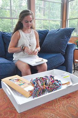 Scores of friendship bracelets in the foreground are ready to be shipped to the international nonprofit Unbound while their creator, Cathedral High School senior Rachel Kent of Indianapolis, makes another to add to the stack. For each bracelet she sells, Rachel makes one for Unbound to give to an impoverished child in a foreign country, and gives all proceeds to the layCatholic founded organization. (Photo by Natalie Hoefer) 