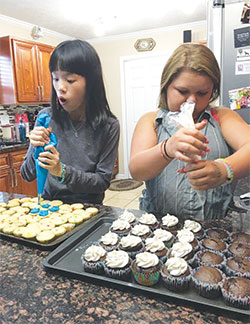 Yiwen Cao, left, and Sara Matthews, a seventh-grader at Seton Catholic High School in Richmond, decorate cupcakes in Sara&rsquo;s home at the start of the 2016-17 academic year. Yiwen was part of a group of Chinese students who visited Seton for about a month. (Submitted photo)