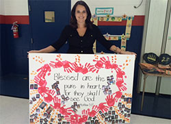 Brittany Geswein holds a canvas that captures her favorite Beatitude and the photos of her students&mdash;past and present&mdash;at St. Mary-of-the-Knobs School. (Submitted photo) 