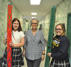 Our Lady of Lourdes middle school teacher Angie Therber and Lourdes eighth-grade students Grace Swinefurth, left, and Olivia Wilson show the &ldquo;peace posts&rdquo; created by the Indianapolis school&rsquo;s eighth graders to promote peace in the school&rsquo;s east side neighborhood. (Photo by Sean Gallagher)