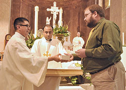 Then-transitional Deacon Nicol&aacute;s Ajpacaj&aacute; gives holy oils to Adam Welp, a member of Holy Family Parish in New Albany, during the archdiocesan chrism Mass on March 22, 2016, in SS. Peter and Paul Cathedral in Indianapolis. Assisting Deacon Ajpacaj&aacute; is then-transitional Deacon Meril Sahayam of the Palayamkottai, India, Diocese. (File photo by Sean Gallagher)