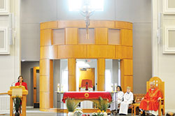 Sharon Albert proclaims the first reading during Palm Sunday Mass while retired Father David Lawler and two altar servers listen in St. Monica Parish&rsquo;s restored and renovated church on April 9. The location of the Blessed Sacrament Chapel behind the altar was one of the changes made to the sanctuary. (Photo by Natalie Hoefer)