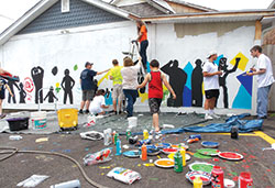 The students of the Missionary Disciples Institute get hands-on service experience helping local children paint a mural on the DAT House, an Indianapolis community center, on June 15. The immersion experience was offered by Marian University in&nbsp;Indianapolis. (Photo by Katie Rutter)