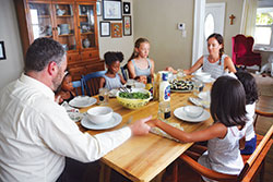 Josh Bach leads his family in a prayer before the meal in their home in Indianapolis on July 10. He and his wife, Cara, members of St. Joan of Arc Parish in Indianapolis, have adopted the three girls seated in the chairs&mdash;Amelia, left, and Frances, both 6, and Victoria, 12. They hope to finalize soon the adoption of the two girls seated on the bench, who for legal reasons must remain anonymous until their adoption is complete. (Photo by Natalie Hoefer)