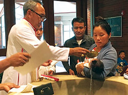 Bishop Lucius Hre Kung of the Diocese of Hakah in Myanmar, left, baptizes Bernadette Ngun, the child of two Myanmar refugees, on July 7 during the bishop&rsquo;s visit to St. Barnabas Parish in Indianapolis. Ngun is held by her mother Monica Shwe, while family friend Robert Hram Hei looks on. (Photo by Patty Cain)