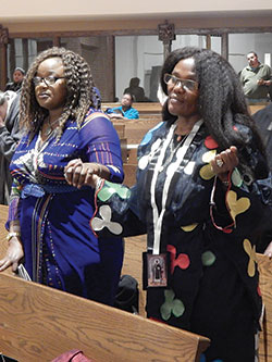 Amaka Ogbuehi, left, and her sister, Nneka Jemie, both natives of Nigeria, hold hands while praying the Lord&rsquo;s Prayer during the Nov. 3 Mass. (Photo by Mike Krokos)