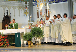 Archbishop Charles C. Thompson, left, prays the eucharistic prayer during a Mass for archdiocesan participants at the National Catholic Youth Conference at St. John the Evangelist Church on Nov. 16. He was assisted by 17 priests of the archdiocese. Shown in this photo are kneeling, Father Patrick Beidelman, left, executive director of the archdiocesan Office of Worship and Evangelization, Fathers&nbsp;Joseph Rautenberg, Douglas Hunter, Jonathan Meyer, Kyle Rodden and Eric Augenstein. (Photo by Natalie Hoefer)	