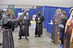 Conventual Franciscan Brother Joseph Martin Huang takes a photo of a National Catholic Youth Conference participant from the Covington, Ky., Diocese standing beside life-size cutouts of St. Francis of Assisi and St. Th&eacute;r&egrave;se of Lisieux on Nov. 16 in the conference&rsquo;s Thematic Village in the Indiana Convention Center in Indianapolis. Looking on are Conventual Franciscan Fathers John Bamman, second from left, and Jijo Thomas. (Photo by Sean Gallagher)