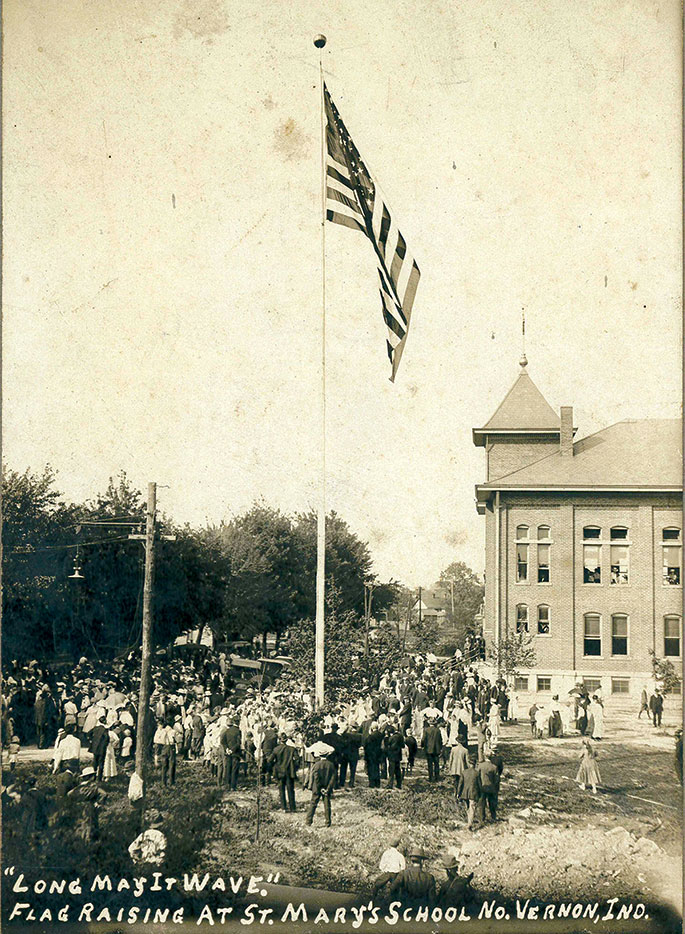 This photo shows a flag raising event at St. Mary School in North Vernon. Though no date is given on the photo, it could depict celebrations related to the dedication of the school building by Bishop Denis O&rsquo;Donoghue, former auxiliary bishop of Indianapolis, on June 21, 1908. St. Mary Parish was founded in 1861, and the school continues to operate in the building shown in this photograph.