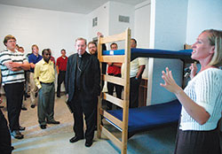 Emily Able, right, director of community and youth services at the archdiocesan Holy Family Shelter in Indianapolis, guides Archbishop&nbsp;Daniel M. Buechlein, center, archdiocesan vocations director Father Eric Johnson, standing behind the archbishop, and a group of archdiocesan seminarians on an Aug. 11, 2010, tour of the shelter for homeless families. (File photo by Sean Gallagher)