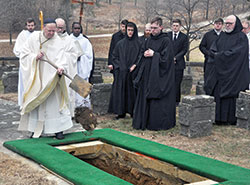 With monks and seminarians looking on, Benedictine Archabbot Kurt Stasiak tosses a spade of dirt onto the casket of Archbishop&nbsp;Emeritus Daniel M. Buechlein on Feb. 1 after it had been lowered into its grave in the cemetery of Saint Meinrad Archabbey in&nbsp;St. Meinrad. (Photo by Sean Gallagher)