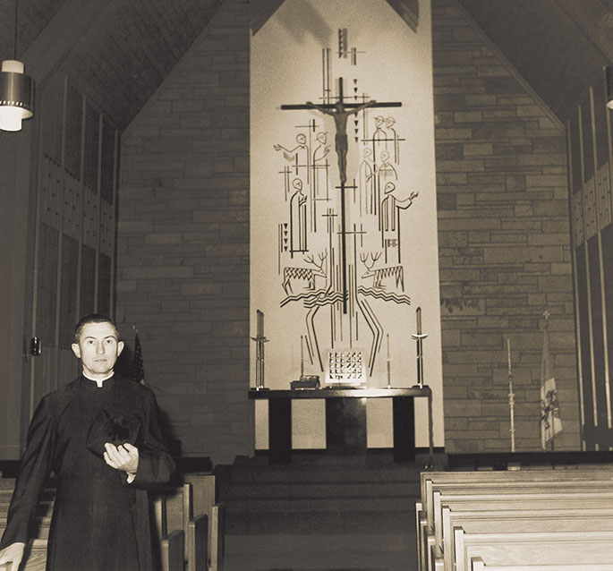 American Martyrs Parish in Scottsburg was founded in 1938, and used a renovated public school as their first church building. In 1963, the parish received funds from the Archdiocesan Home Missions Fund to construct a new church. In this photo, Father William Engbers, pastor, is shown with a mural depicting Christ and the American Martyrs in the new church building, a few days before its dedication on April 19, 1964.