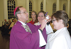 As part of administering the sacrament of confirmation, Archbishop Charles C. Thompson prepares to make the sign of the cross with sacred chrism oil on the forehead of Marguerite Engle during a Mass at the Indiana Women&rsquo;s Prison chapel in Indianapolis on the evening of March 4. Engle and Opal Williams, third from left, received the sacraments of baptism, confirmation and the Eucharist during the Mass. In the background, Andrea Wolsifer of St. Anthony Parish in Indianapolis watches the two women whom she guided through the Rite of Christian Initiation of Adults to be received into the full communion of the Church. (Photo by John Shaughnessy)