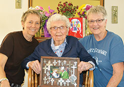Just days after her 109th birthday, Mary Weir, center, of St. Thomas the Apostle Parish in Fortville, poses in her home with her granddaughter, Paige&nbsp;Hunt, left, and her daughter, Peggy Hunt, who both help care for Weir. The centenarian proudly displays a photo of her meeting then‑Archbishop&nbsp;Joseph W. Tobin in 2016. (Photo by Natalie Hoefer)