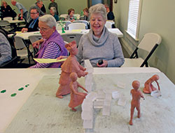 At the Cardinal Ritter House annual Irish coffee lecture on March 15, Janice Cooley, right, and Joan Gilley inspect Guy Tedesco&rsquo;s clay model of a planned lawn sculpture group of Cardinal Joseph E.&nbsp;Ritter and children pulling down a wall symbolic of discrimination. Both are members of Our Lady of Perpetual Help Parish in New Albany. (Photo by Patricia Happel Cornwell)