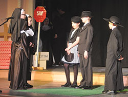 Students of St. Joseph School in Shelbyville act on March 19 in a scene from the St. Joe Show at the Strand Theater in Shelbyville, a play about the founding of St. Joseph Parish written by its administrator, Father Michael Keucher. The students playing Franciscan sisters are Macey&nbsp;Robbins, left, Leah Smothers and Molly Johnson. Taylor Abell and Tyler Gwinnup, center, act as the mayor of Shelbyville and his wife, and Charlie Fischer, at right, plays Father Francis Rudolf, founder of St.&nbsp;Joseph School and the parish&rsquo;s first resident pastor. (Photo by Sean Gallagher)