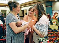 Julie Alumbaugh shows her 2-week-old daughter to her mother Cathy McMahon, center, and twin sister Mary Warren at the Indiana Catholic Women&rsquo;s Conference on March 10 in Indianapolis. The theme of the conference was &ldquo;The Sanctification of the Family.&rdquo; (Photo by Victoria Arthur)
