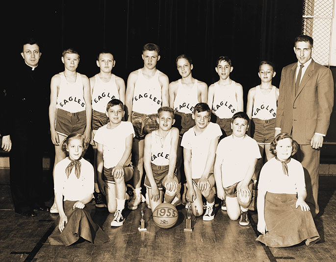 Shown here are the 1955 Eagles basketball team and cheerleaders from the former St. John the Evangelist Parish in Enochsburg. The priest at left is Father Ambrose Schneider, longtime pastor of the Batesville Deanery faith community. According to a note on the back of the photo, the team won the Franklin County tournament that year. The former St. John the Evangelist Parish merged with the former St. Maurice Parish in Decatur County in 2014. St. Catherine of Siena Parish in Decatur County was then formed from the two previous parishes.