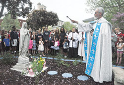 With students of St. Joan of Arc School looking on, Father Guy Roberts, pastor of St. Joan of Arc Parish in Indianapolis, blesses on May 3 a newly created rosary garden on the parish&rsquo;s grounds. The school&rsquo;s seventh- and eighth-grade classes created the garden through a grant from Queen&nbsp;and Divine Mercy Center Endowment Fund, managed by the archdiocesan Catholic Community Foundation. (Photo by Sean Gallagher)