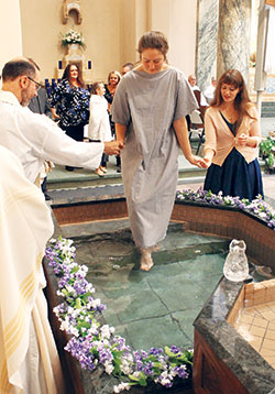 Catechumen Hannah Bach, 18, is guided into the baptismal font at St.&nbsp;Joseph University Church in Terre&nbsp;Haute by Conventual Franciscan Father Mark Weaver, the parish&rsquo;s pastor, and her sponsor Sierra Flores during the Easter Vigil Mass on March 31. (Submitted photo by Bill Foster)