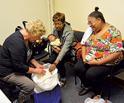 Birthline volunteer Barbara Lemen, left, China Jones, middle, and Janeane Jones admire a hand-crocheted blanket for China&rsquo;s 6-week-old son at the Archbishop Edward T. O&rsquo;Meara Catholic Center in Indianapolis on Oct. 10. (Photo by Natalie Hoefer)