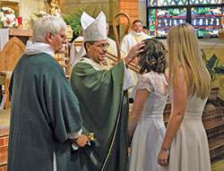 Archbishop Charles C. Thompson anoints the head of Lexie Curl during the sacrament of confirmation at St. Mary Church in Lanesville on Oct. 13. He is assisted by Deacon Richard Cooper, left, while Lexie&rsquo;s sponsor Kaylee Wheatley, right, looks on. The Mass also celebrated the 175th&nbsp;anniversary of the parish&rsquo;s founding. (Photo by Natalie Hoefer)