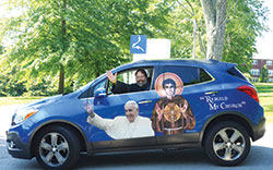 Conventual Franciscan Father John Bamman smiles and waves from his 2014 Buick Encore, the vehicle that he drives across the Midwest&mdash;with Pope&nbsp;Francis and St. Francis at his side&mdash;to promote vocations. (Submitted photo)