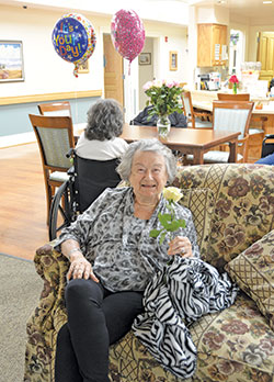 A resident&mdash;or elder, as residents are respectfully referred to at Guerin Woods retirement care community&mdash;shows off a rose she received as part of a birthday celebration for the elder seated behind her in one of the community&rsquo;s villas on Oct. 13. (Photo by Natalie Hoefer)