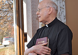 In this photo from Nov. 27, 2013, retired Father&nbsp;Herman Lutz, gazes out of the main parlor window of St.&nbsp;Paul Hermitage in Beech Grove, the retirement home where he and three other retired archdiocesan priests reside. (Photo courtesy of the archdiocesan Office of Stewardship and Development)
