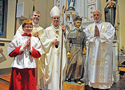 Altar server John Crawley, left, Father Jonathan Meyer, Archbishop Charles C. Thompson and Deacon Robert Decker pose on Nov. 6 in St. Paul Church in New Alsace, a campus of All Saints Parish in Dearborn County, after a Mass in which Archbishop Thompson blessed a statue of the Servant of God Bishop Simon Brut&eacute;. Deacon Decker carved the statue. John built a shrine for the statue in the church, which was dedicated by Bishop Brut&eacute; in 1838, for an Eagle Scout project. (Photo by Sean Gallagher)