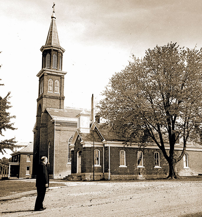 In this photo from 1966, Father Robert Wilhelm is seen near St. Ann Church in Jennings County. The parish was founded in 1841. The brick church building, still in use, was constructed in 1866 and succeeded an original log structure. Father&nbsp;Wilhelm was the pastor of St. Ann Parish, as well as the former St. Denis Parish in Jennings County, from 1957-67. 
