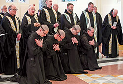 With monks of Saint Meinrad Archabbey standing behind them, Benedictine Brothers Simon Herrmann, left, Nathaniel Szidik, Joel Blaize and Jean Fish kneel in prayer during a Jan. 25 liturgy at the Archabbey Church of Our Lady of Einsiedeln in St. Meinrad in which the brothers professed solemn vows. In a ritual symbolizing humility, monks of Saint Meinrad who profess solemn vows have all of their hair cut off except for a small band that is traditionally called in Latin a &ldquo;corona&rdquo; (&ldquo;crown&rdquo;). (Photo courtesy of Saint Meinrad Archabbey)