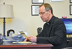 Archbishop Charles C. Thompson reads one of more than 1,000 prayer intentions stacked on his desk that have been sent in so far with this year&rsquo;s United Catholic Appeal pledge intentions and payments. He reads and prays for the intentions each year. Usually there are less than 100 requests. (Photo by Natalie Hoefer)
