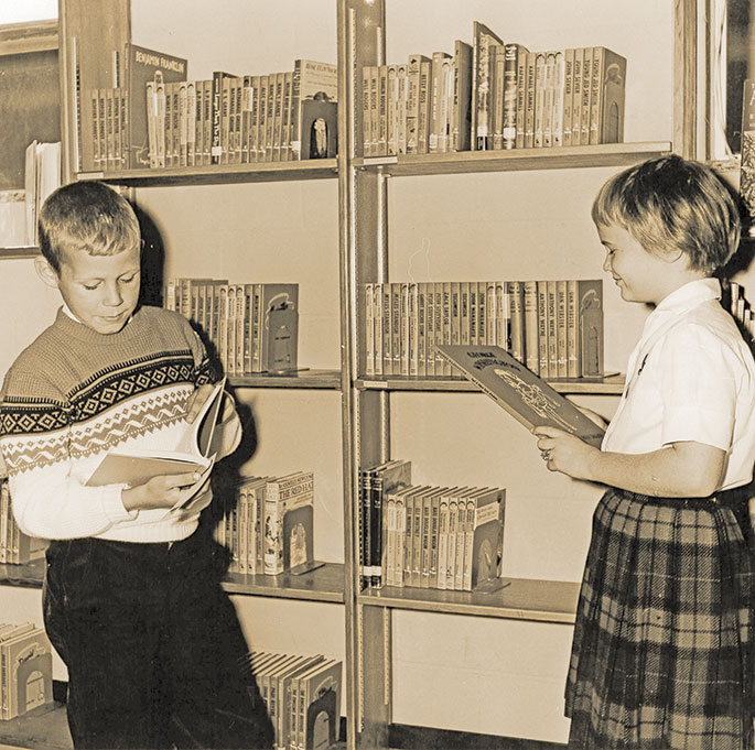 In this photo, Tim Fox and Irma Noel peruse the biography section of the library at the St. Luke the Evangelist School in Indianapolis. The photo was published in the St. Luke the Evangelist Church dedication souvenir booklet from Oct. 22, 1961. The booklet notes that the school library contained 1,200 books at that time. St. Luke Parish was established on Sept. 2 of that same year, and the school, which had already been under construction, opened a few days later.