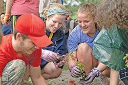 Clare Stephens, center, a mentor at the Missionary Disciples Institute hosted by Marian University in Indianapolis, plants flowers outside the Unleavened Bread Caf&eacute; in Indianapolis with Elizabeth Reed, right, a student at St.&nbsp;Louis Catholic High School in Lake Charles, La., on June 20. The activity aimed to help the young people become acquainted with the members of the caf&eacute;, which was founded as a community space for women who had been formerly incarcerated, addicted to drugs, or experienced other difficult circumstances. (Photo by Katie Rutter)