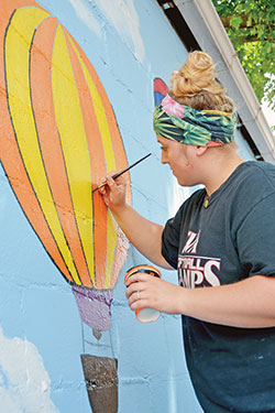 Alex Moehn of Kimberly, Wis., paints a mural for the children&rsquo;s play area on the St. Elizabeth Catholic Charities campus in New Albany on June 19. (Photo by Natalie Hoefer)