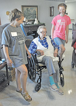 Catholic HEART Workcamp participants Felicia Samuels, left, and Sarah Pottorff, both of West&nbsp;Dundee, Ill., perform dance moves with a resident of the Little Sisters of the Poor&rsquo;s St.&nbsp;Augustine Home for the Aged in Indianapolis on June 11. (Photo by Sean Gallagher)