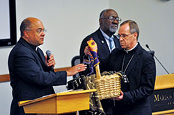 Archbishop Charles C. Thompson holds a basket containing written accounts of experiences of racism being blessed by Bishop Shelton J. Fabre, chairman of the U.S. bishops&rsquo; Ad Hoc Committee against Racism, during a listening session on racism held at Marian University in Indianapolis on Sept. 30. Fifteen Catholics from across central and southern Indiana told the stories of their experiences of racism at the event that drew approximately 100 attendees. Holy Cross Brother Roy Smith, center, served as master of ceremonies for the session. (Photo by Sean Gallagher)