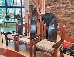 Father Sean Danda, pastor of St. Malachy Parish in Brownsburg, stands proudly with the three sanctuary chairs custom-designed and built by parishioners in time for the parish&rsquo;s feast day Mass in November 2018 during the faith community&rsquo;s sesquicentennial year. The artisans volunteered at least 1,600 hours on the project. (Submitted photo)