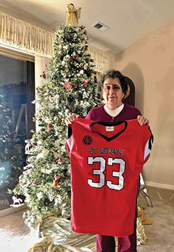 Mary Devine shows the football jersey that she received from the fifth-and-sixth grades&rsquo; football team of St. Lawrence Parish in Indianapolis. The team gave her the jersey after the Nov. 20 funeral Mass for her husband, Patrick Devine, who had coached boys at the parish for 40 years. (Submitted photo)
