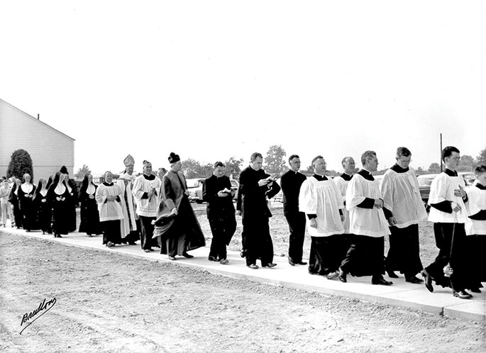 In this photo from Aug. 28, 1955, priests, Sisters of Providence and parishioners of Nativity of Our Lord Jesus Christ Parish in Indianapolis process from the church to the new school on the occasion of its dedication. Archbishop Paul C. Schulte can be seen near the rear of the procession. The original church building, which appears in the background of this photo, was destroyed by fire on Nov. 17, 1965.