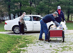 Ryan Borden, middle, and Nick Kleaving, left, both members of the Knights of Columbus of St. Isidore the Farmer Parish in Perry County, help fellow parishioner Ramona Gehlausen, manager of the parish&rsquo;s Martin&rsquo;s Cloak ministry, distribute food on May 2 at the the parish&rsquo;s St. Martin campus in Siberia. (Submitted photo)